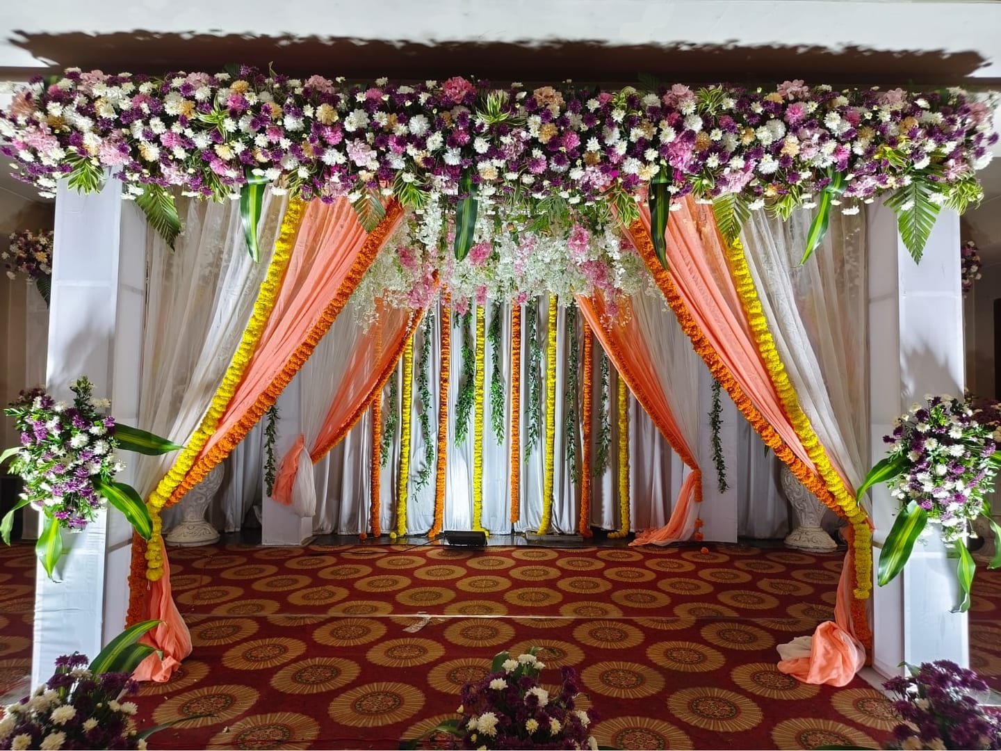 A wedding mandap in marigold and peach drapes with a floral canopy, Sri Sai Convention Hall, Jayanagar